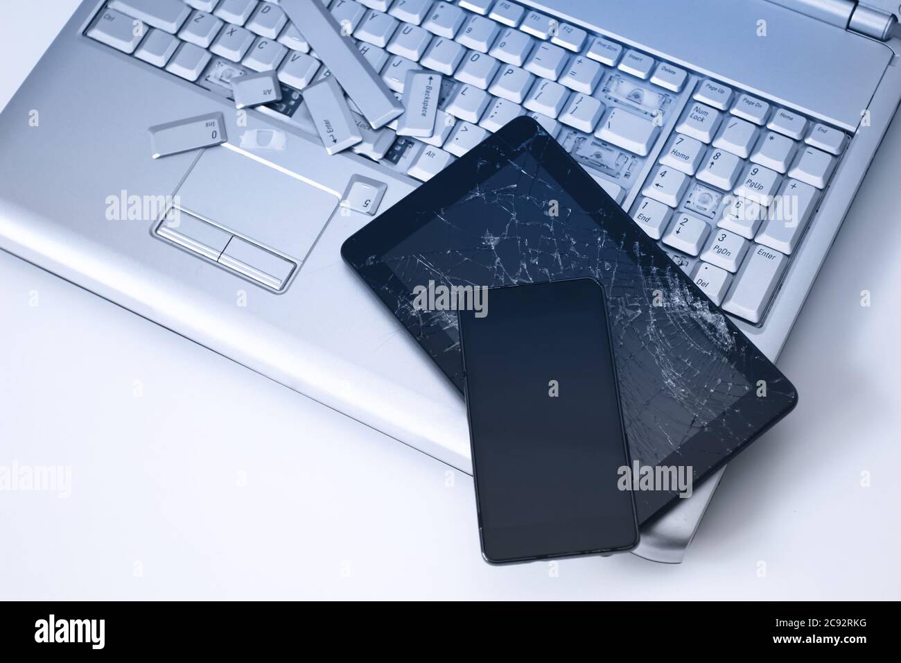 Un computer portatile color argento con tastiera rotta, un tablet con  schermo rotto e un telefono nero. Un'immagine ravvicinata di parte del  computer portatile rotto e dello schermo rotto Foto stock -