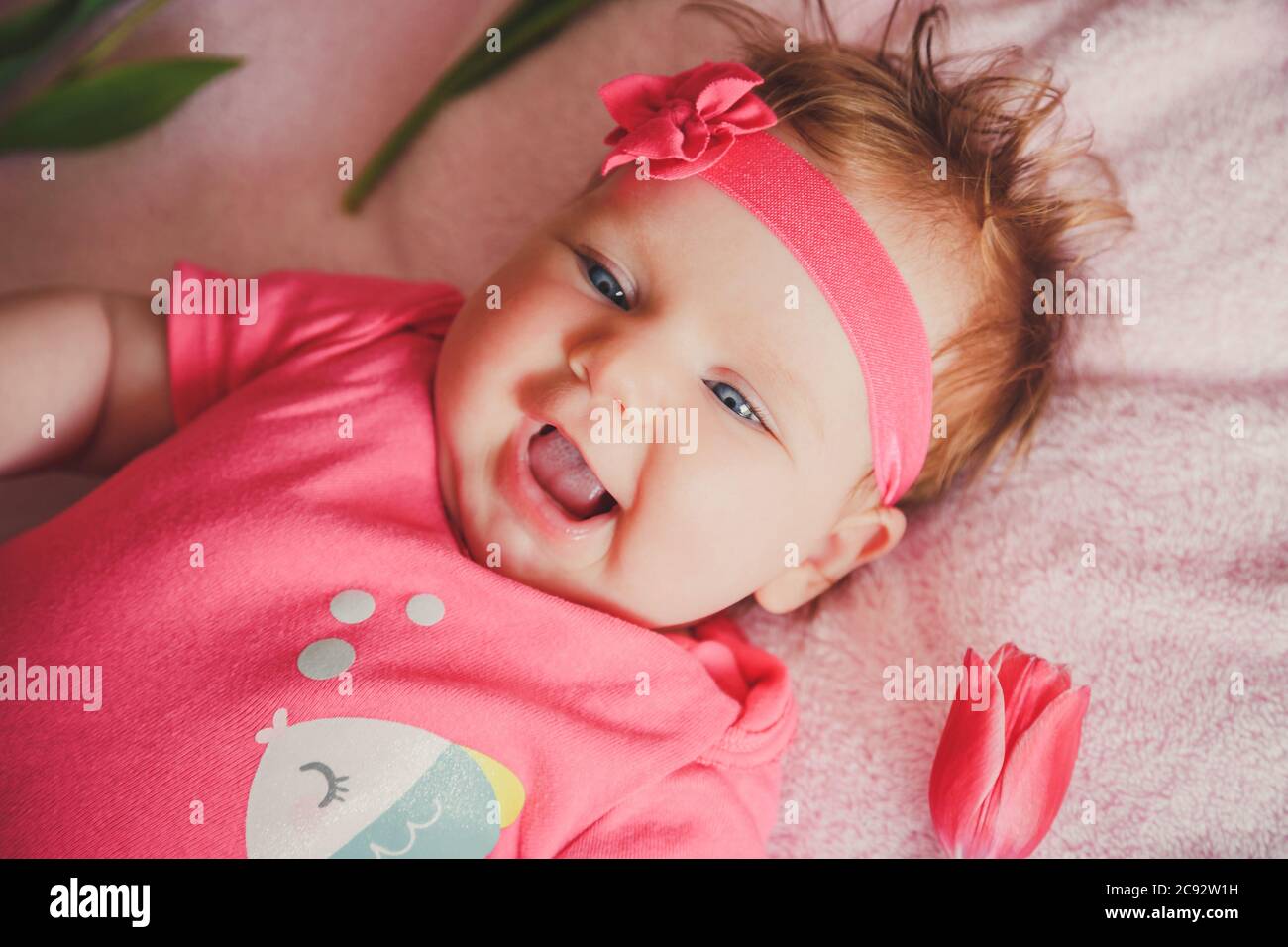 Primo piano ritratto di simpatica ragazza sorridente felice sdraiata sul letto rosa con tulipani intorno. Foto Stock