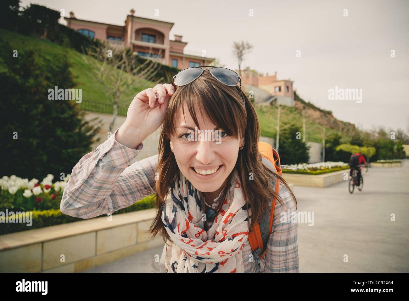 Giovane ragazza sorridente felice in camicia rosa e ancore sciarpa con occhiali da sole sulla testa e zaino arancione guardando la fotocamera all'aperto. Stile di vita sano Foto Stock