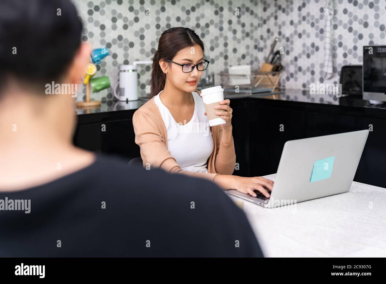 Donna asiatica lavoro da casa in cucina bere togliere il caffè mentre l'uomo lavoro a distanza in primo piano, mentre la città di blocco da coronavirus covid-19 pa Foto Stock