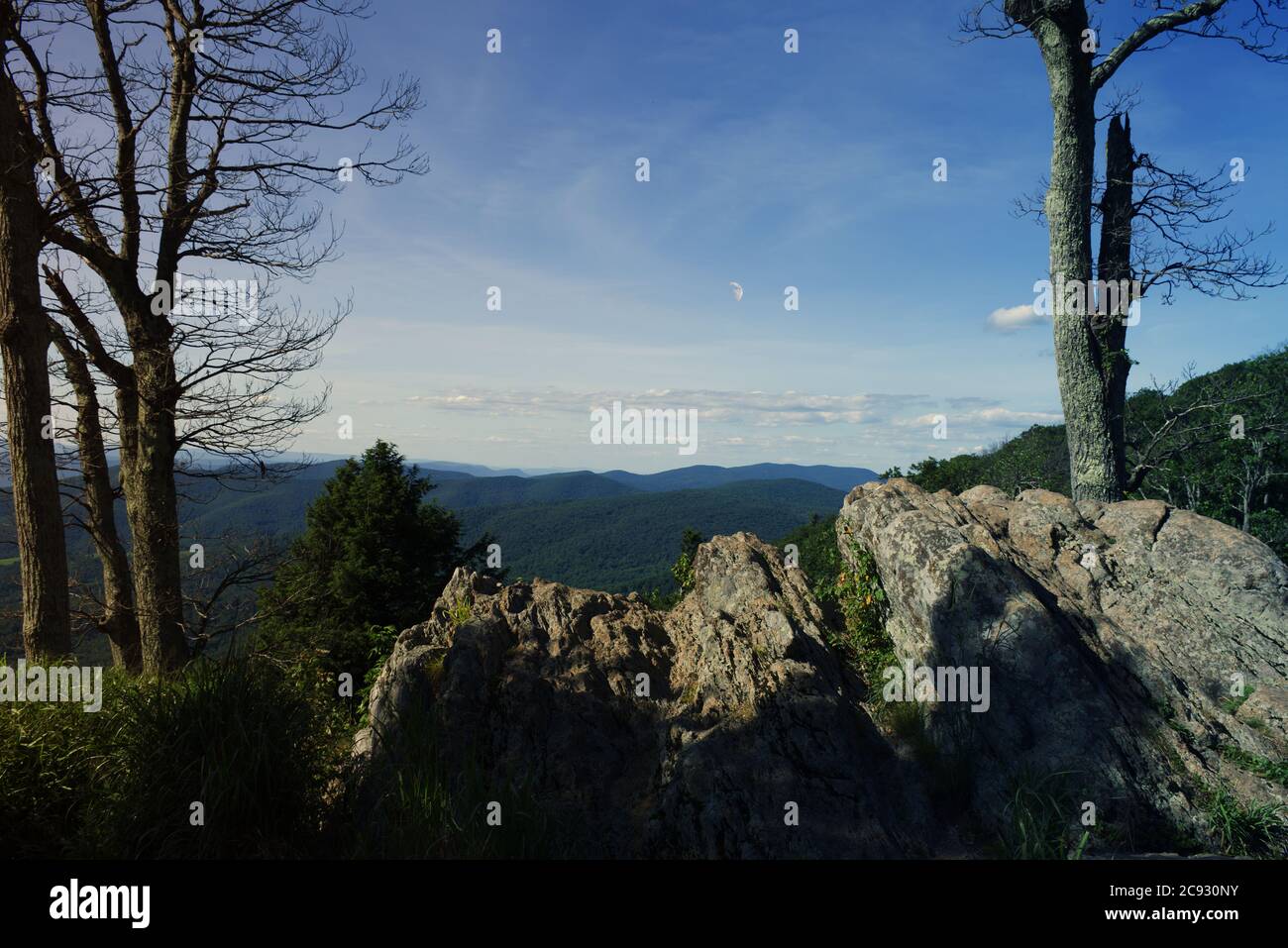 La luna di giorno è visibile in questa immagine da un punto di vista nel parco nazionale di shenandoah che ha scogli e alberi dentellati in primo piano e la copertura dell'albero Foto Stock