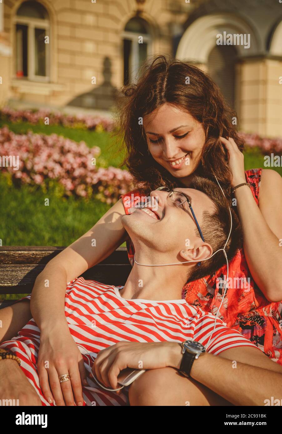 Felice coppia amorevole con gli auricolari che condividono la musica da uno smartphone e abbracciano l'estate all'aperto Foto Stock