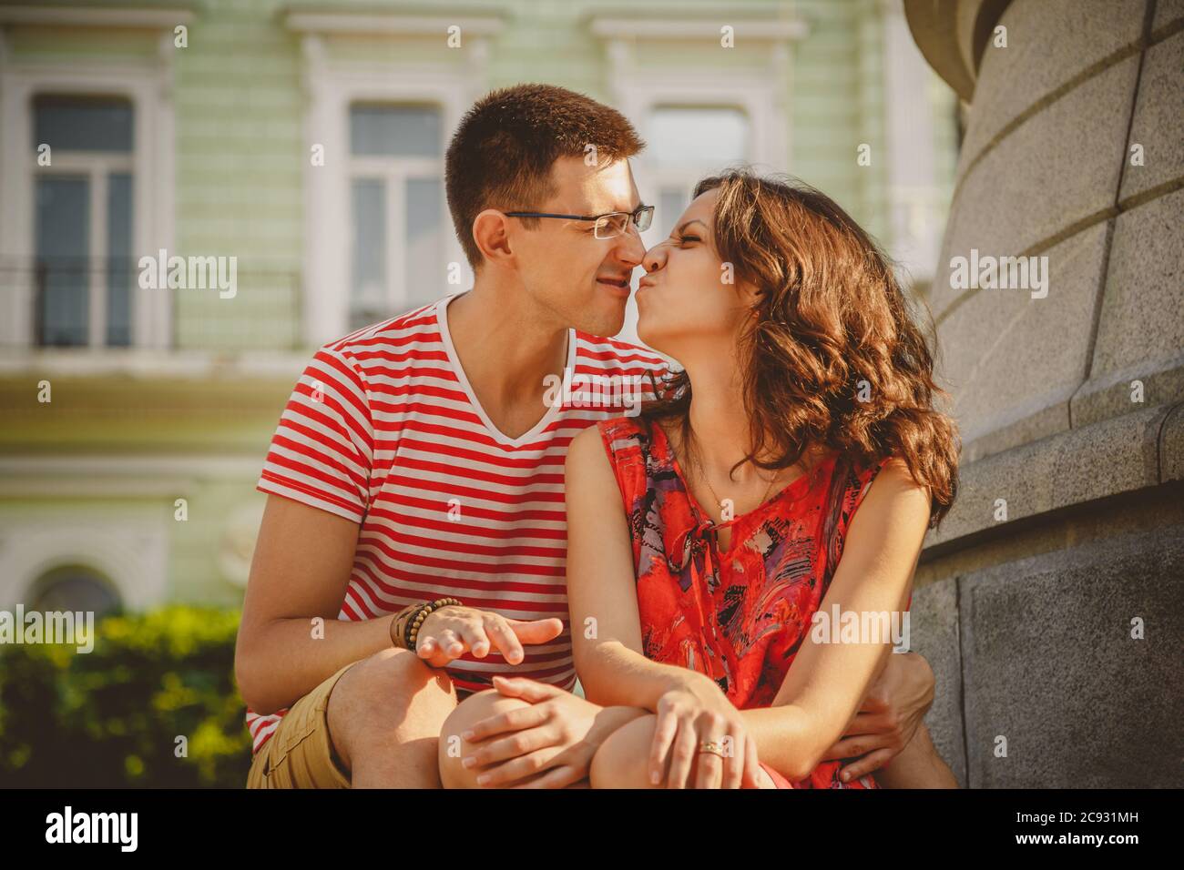 Carino giovane coppia sorridente in amore che tocca i nasi, abbracciando, seduto all'aperto in verde strada della città, in estate Foto Stock