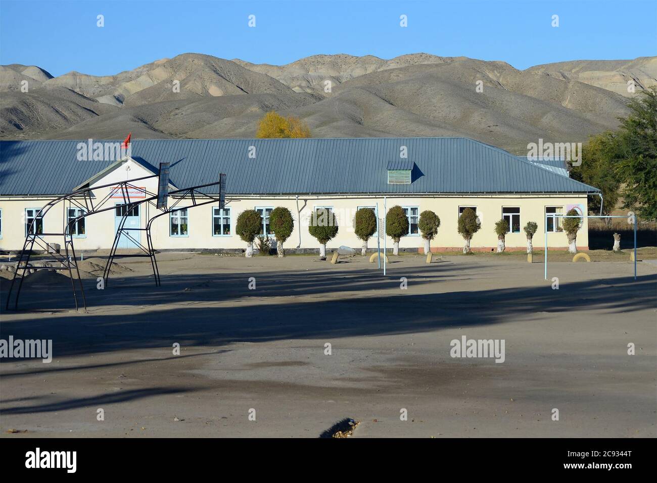 Scuola elementare a Kara-Koo, un piccolo villaggio nella regione di Issyk-Kul nella campagna kirghiza. Area sportiva vuota visibile. Piccolo edificio educativo. Foto Stock
