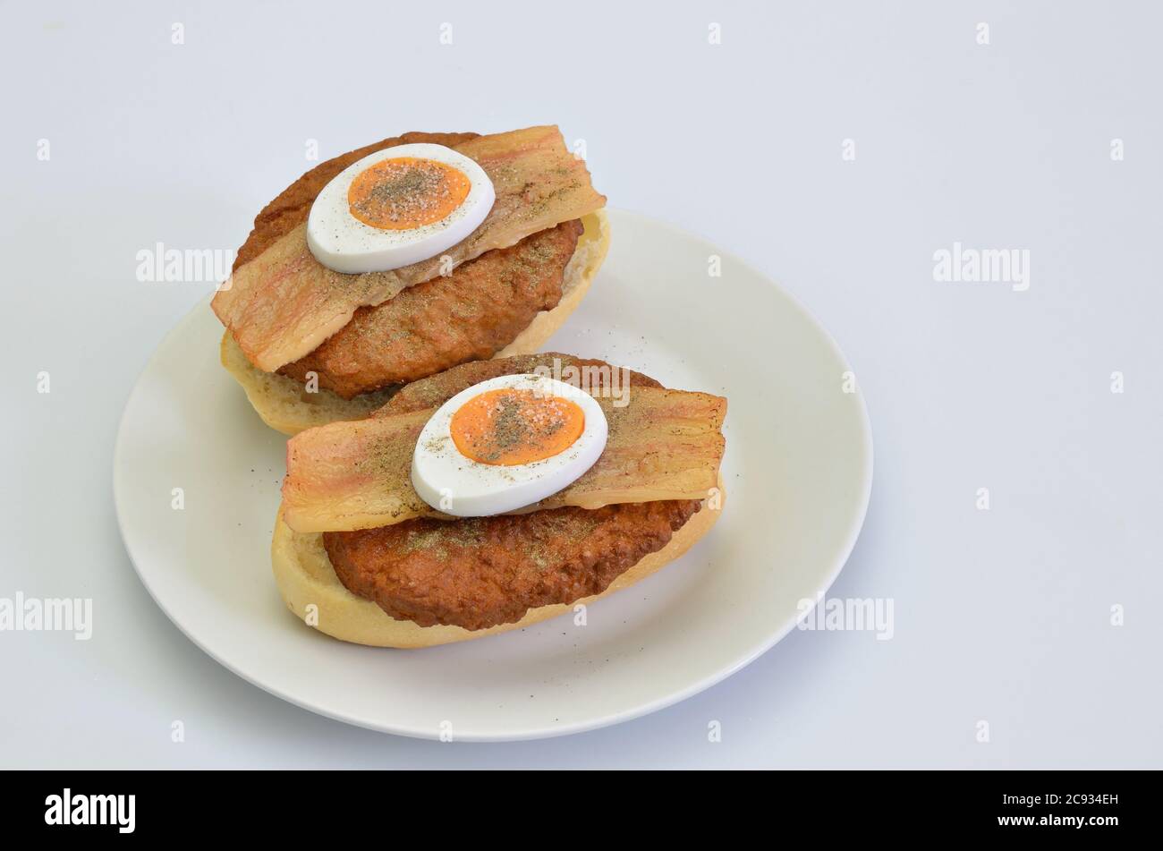 due panini con manzo, pancetta e uovo con sale e pepe su piatto bianco, guardaroba, isolato su fondo bianco Foto Stock