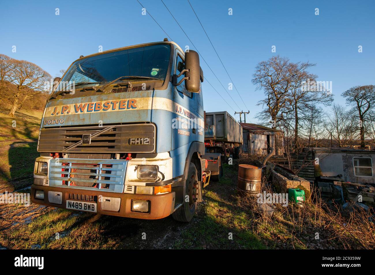 Veicoli Volvo FH12 in disuso e rimorchi con cassone ribaltabile parcheggiati in un'azienda agricola in collina nel distretto di Derbyshire Peak Foto Stock