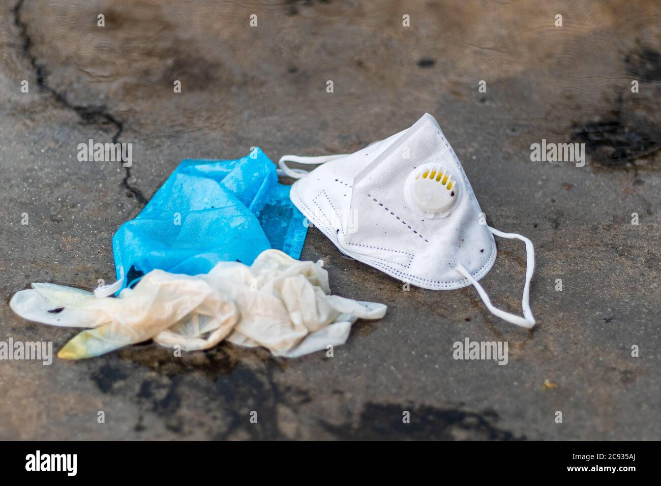 COVID-19 concetto di rifiuti o rifiuti. Guanti scartati, maschera medica e maschera N95 gettati via dopo l'uso sotto la pioggia all'aperto. Foto Stock