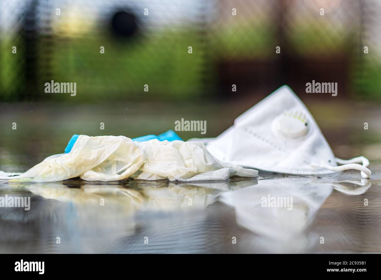 COVID-19 concetto di rifiuti o rifiuti. Guanti scartati, maschera medica e maschera N95 gettati via dopo l'uso sotto la pioggia all'aperto. Foto Stock