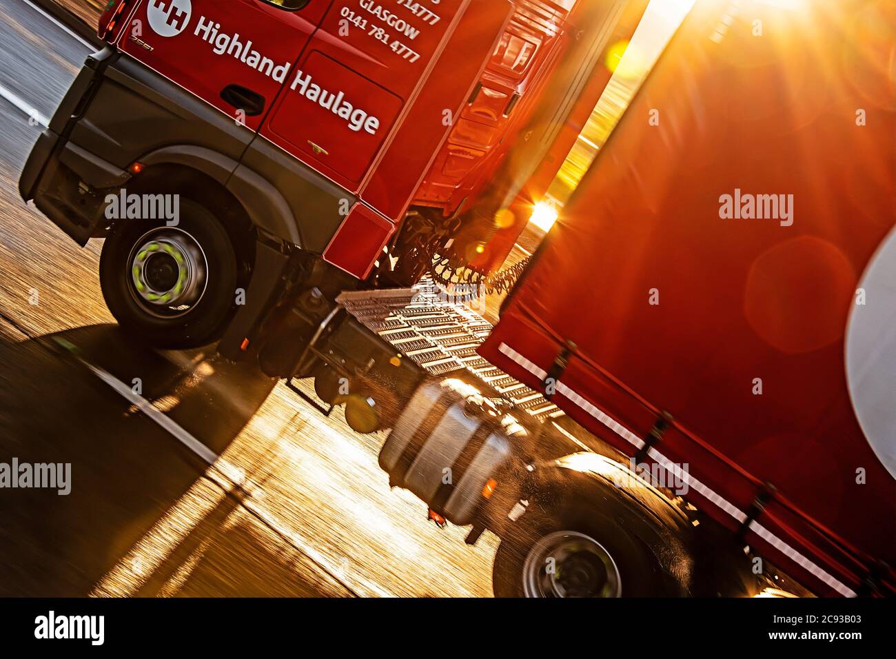 Primo piano di ruote per autocarri pesanti (Mercedes-Benz Actros), retroilluminate dal sole, che guidano lungo una doppia carreggiata sotto la pioggia. Foto Stock