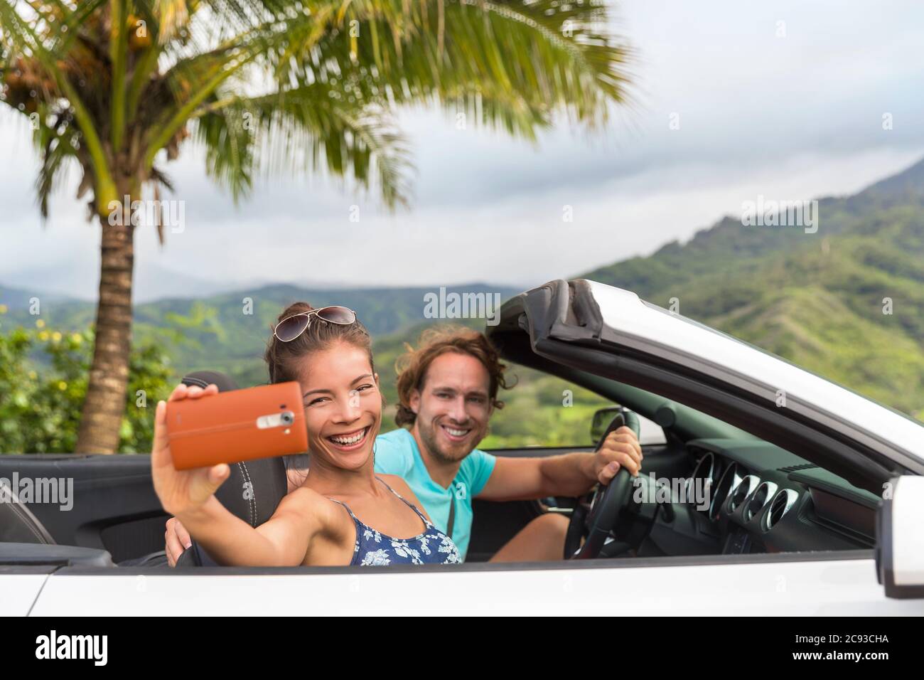 Selfie vacanze auto. Coppia che si diverte durante il viaggio estivo facendo foto con smartphone durante il viaggio. Giovani multirazziali che guidano Foto Stock