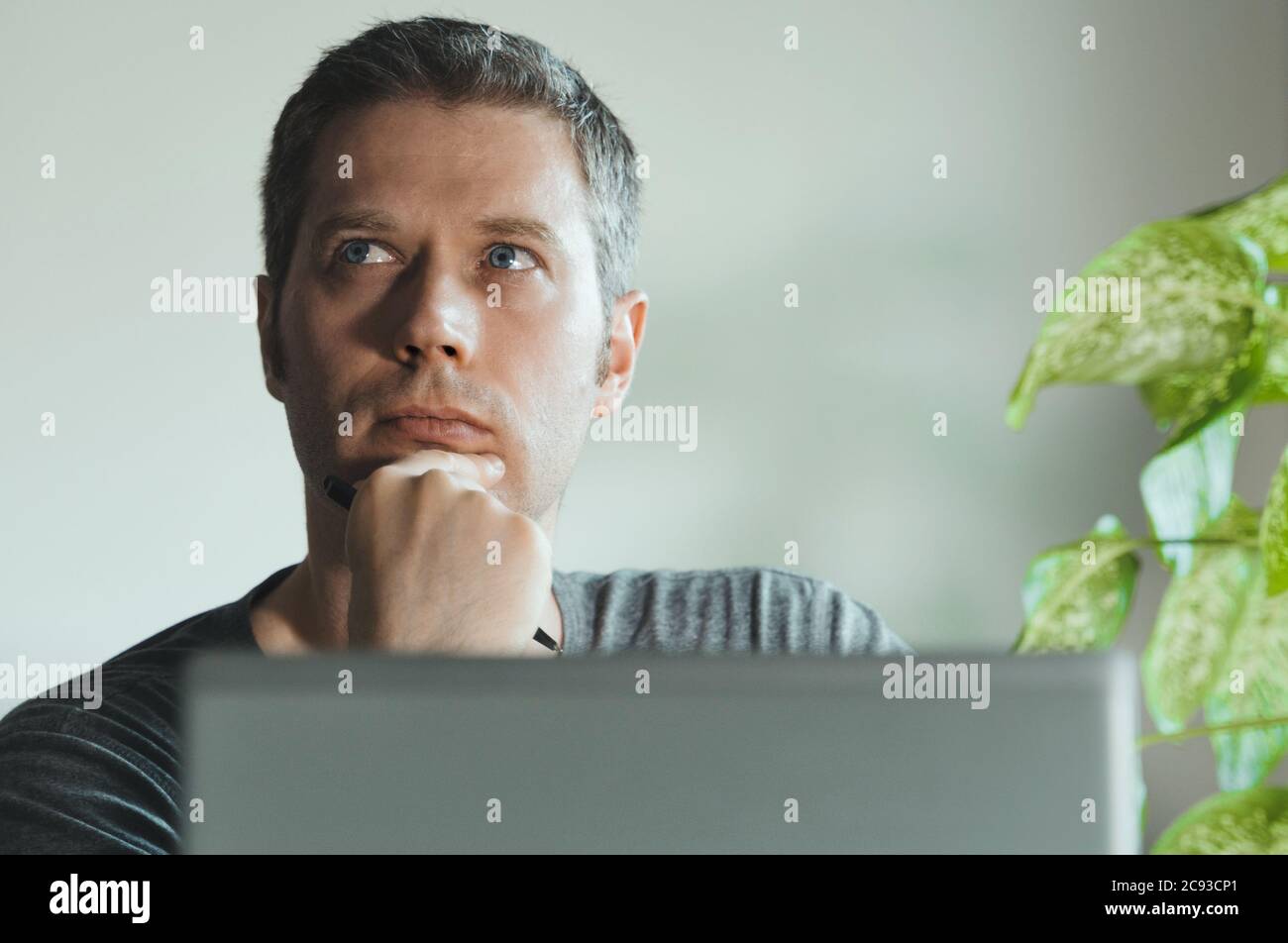 Bell'uomo pensieroso davanti al suo laptop in ufficio. Foto Stock