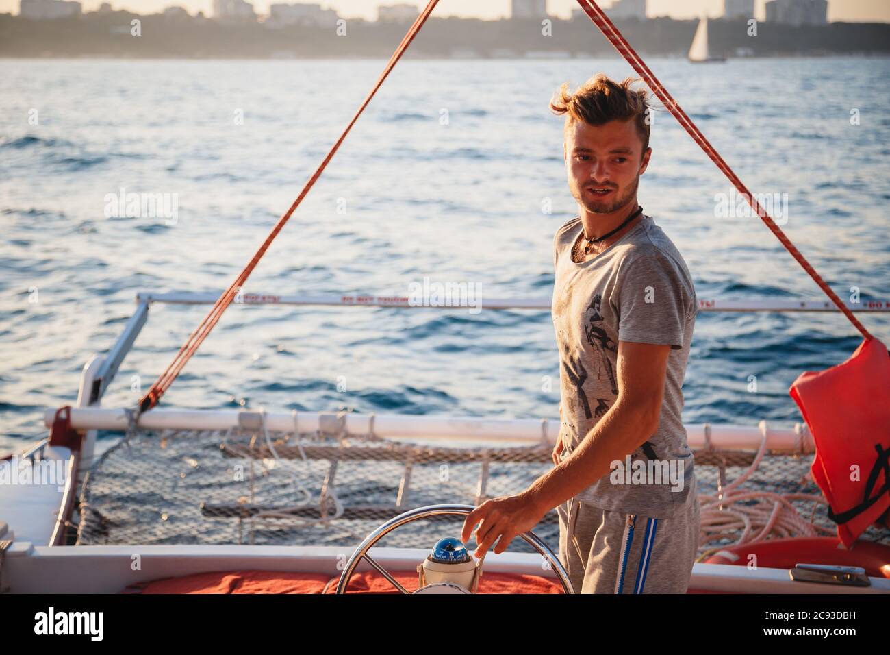 Giovane bell'uomo, capitano che guida yacht in mare in giornata di sole Foto Stock