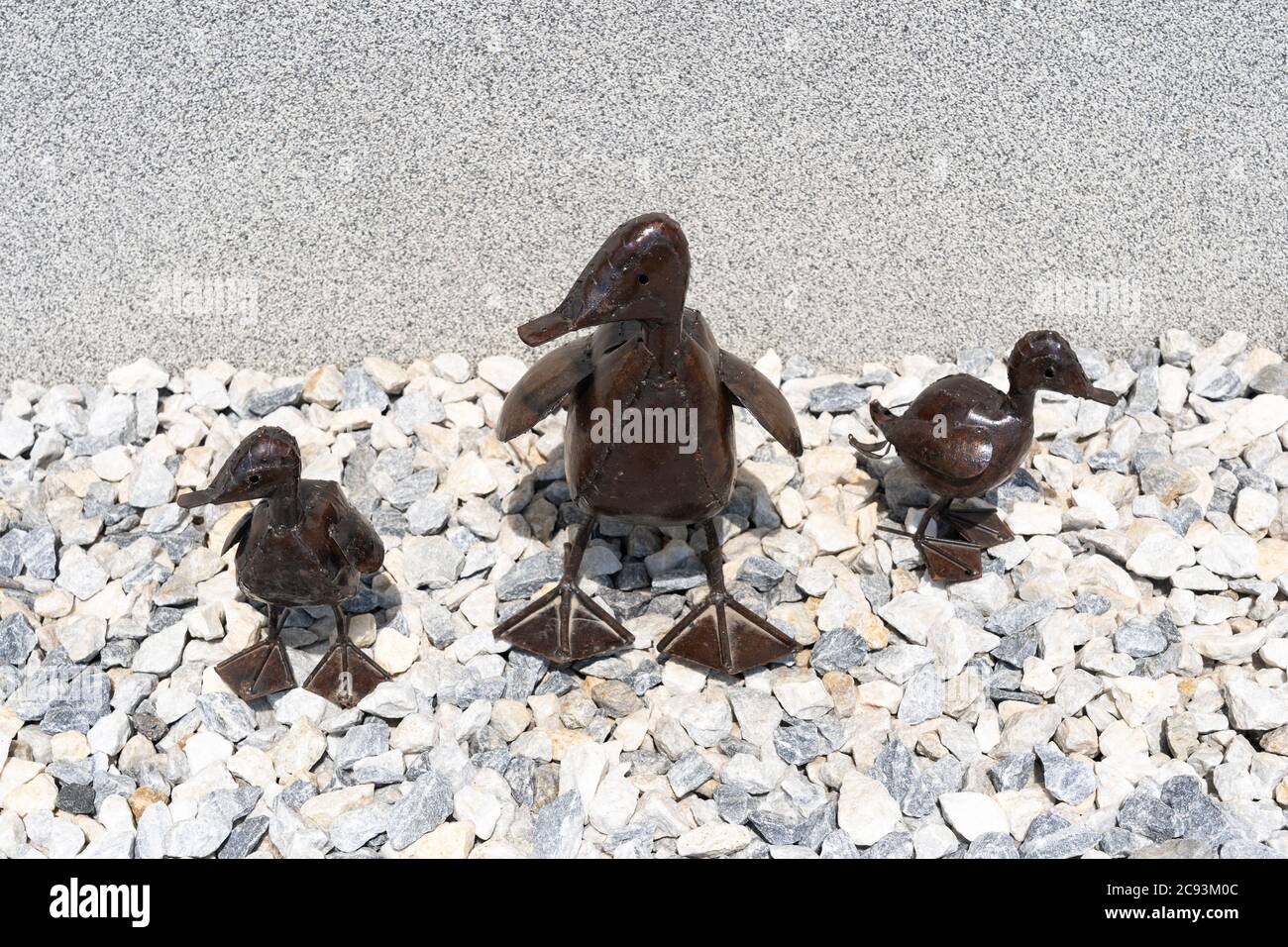 Una mummia e due sculture d'arte decorativa d'anatra del bambino in metallo riciclato in piedi su pietre in un giardino, Regno Unito Foto Stock