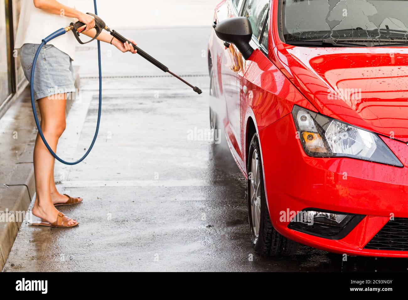 Lavaggio auto. Pulizia dell'auto con acqua ad alta pressione. Auto elettrica rossa. Foto Stock