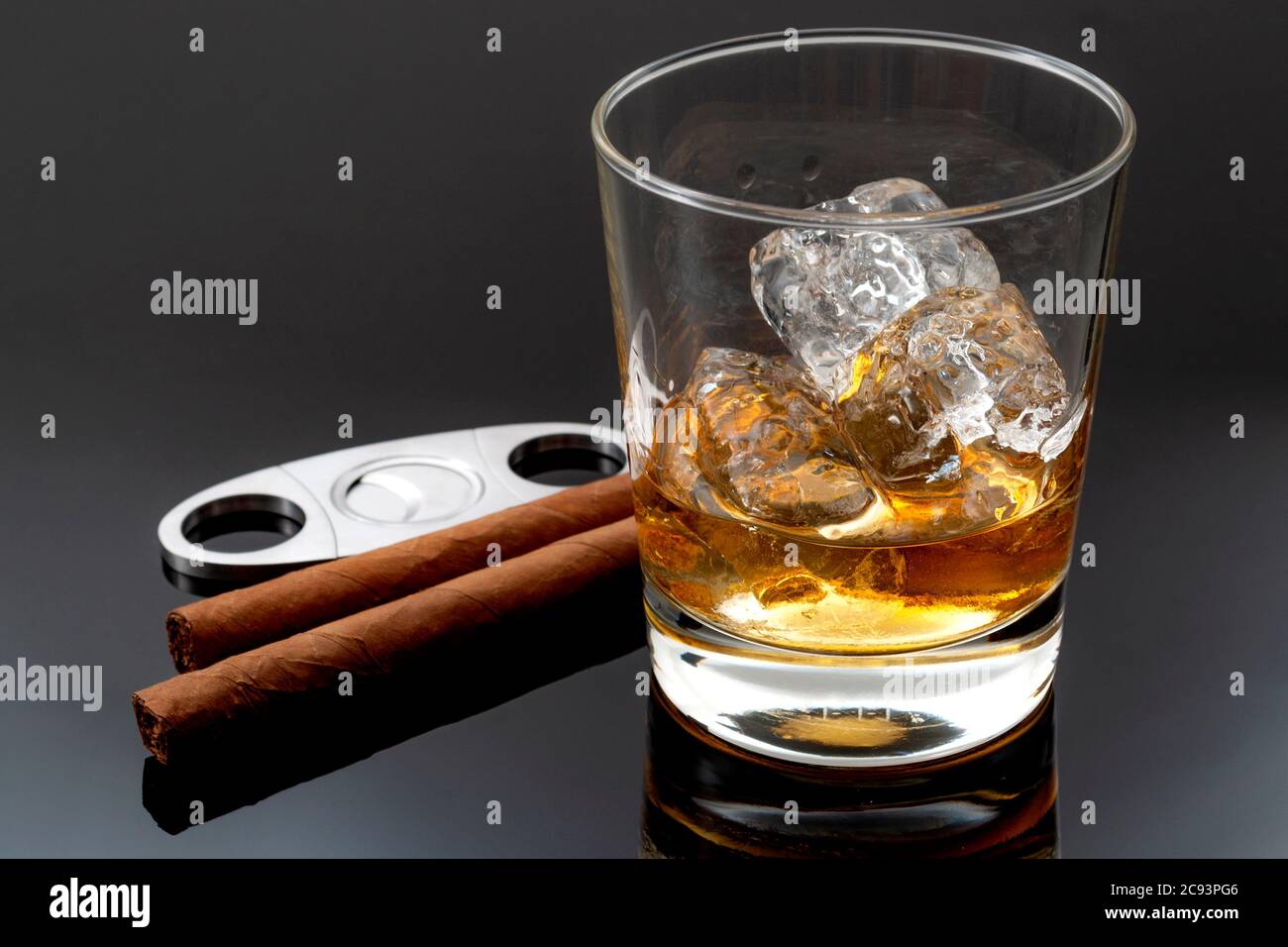 Fumo di tabacco e alcol concetto di bere con bicchiere di whisky sulle rocce, sigari, tagliasigari in metallo e ghiaccio su sfondo scuro Foto Stock