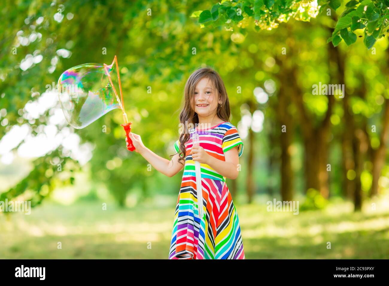Felice bambina bruna gioca con le bolle di sapone estivo nel parco. Stile di vita per bambini Foto Stock