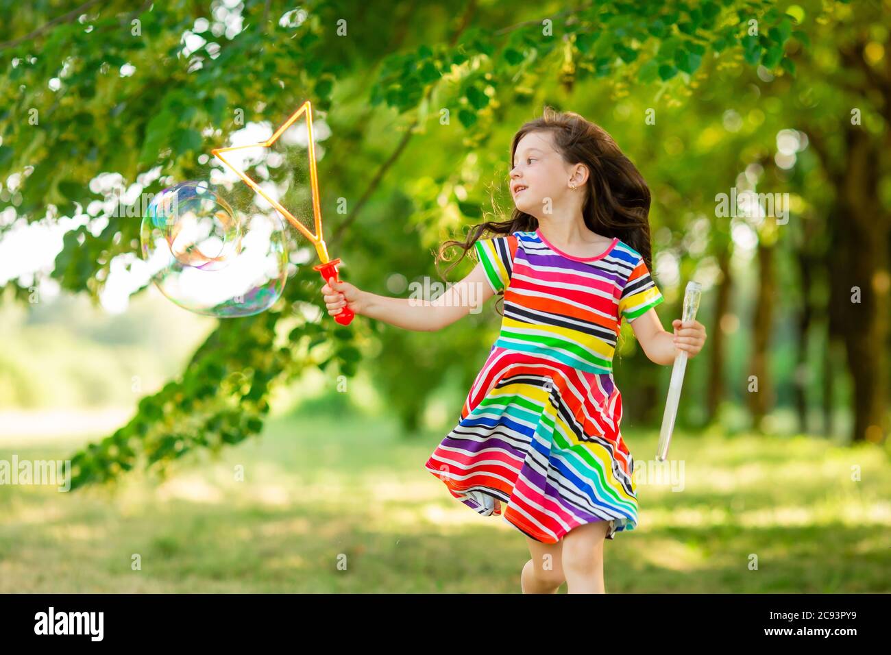 Felice bambina bruna gioca con le bolle di sapone estivo nel parco. Stile di vita per bambini Foto Stock