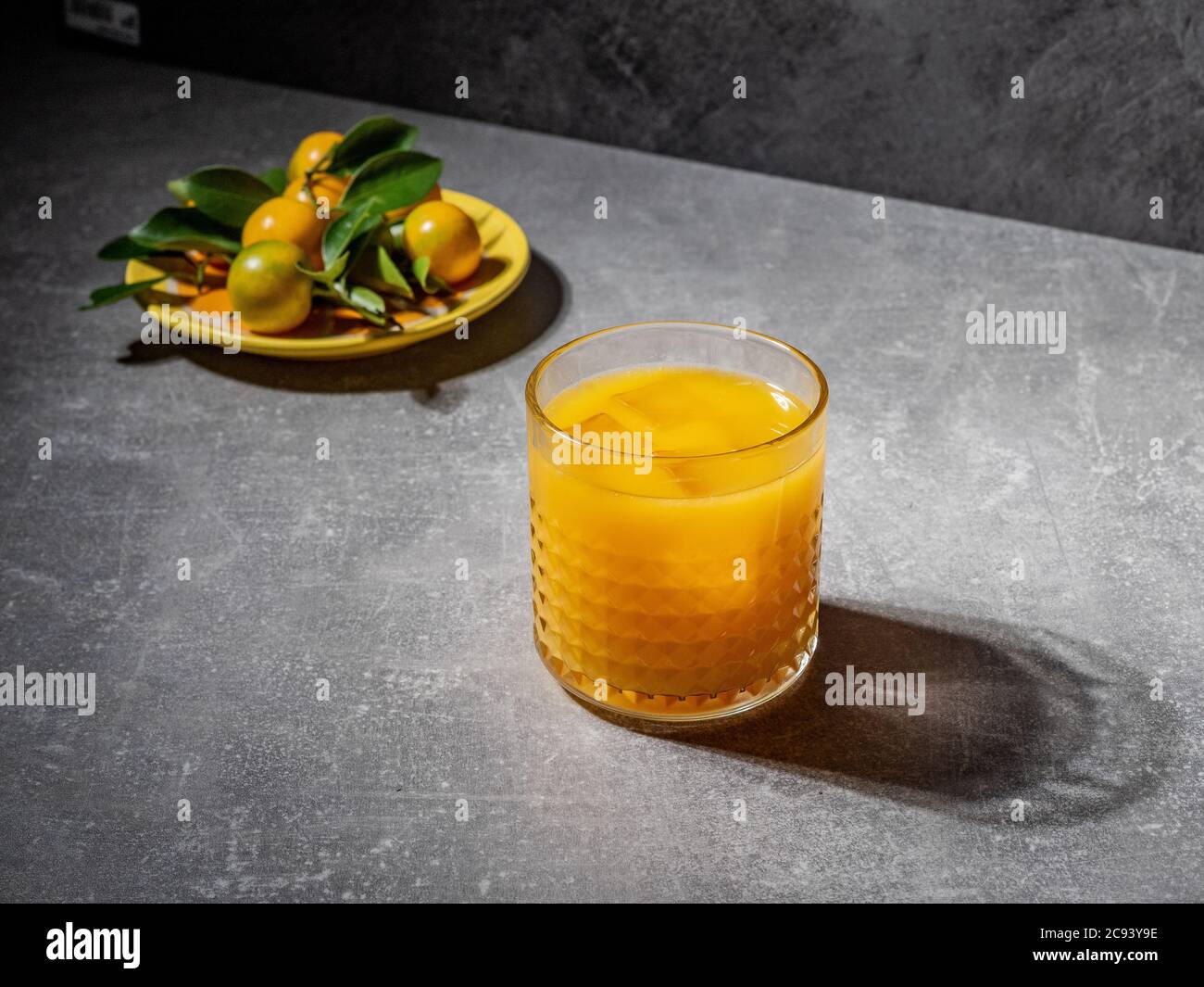 Tangerini con foglie verdi e succo di mandarino fresco in condizioni di forte illuminazione. Scatto in testa. Minimalismo alimentare. Foto Stock