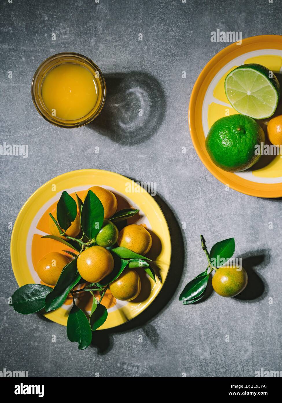 Tangerini con foglie verdi e succo di mandarino fresco in condizioni di forte illuminazione. Foto a soffitto con spazio per la copia. Minimalismo alimentare. Foto Stock