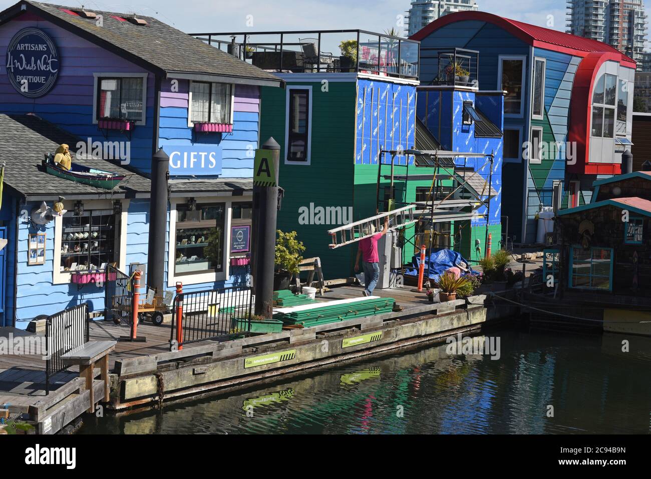 Un operaio porta una scala accanto a un negozio di articoli da regalo galleggiante e galleggianti al Fisherman's Wharf di Victoria, British Columbia, Canada, sull'isola di Vancouver. Fi Foto Stock