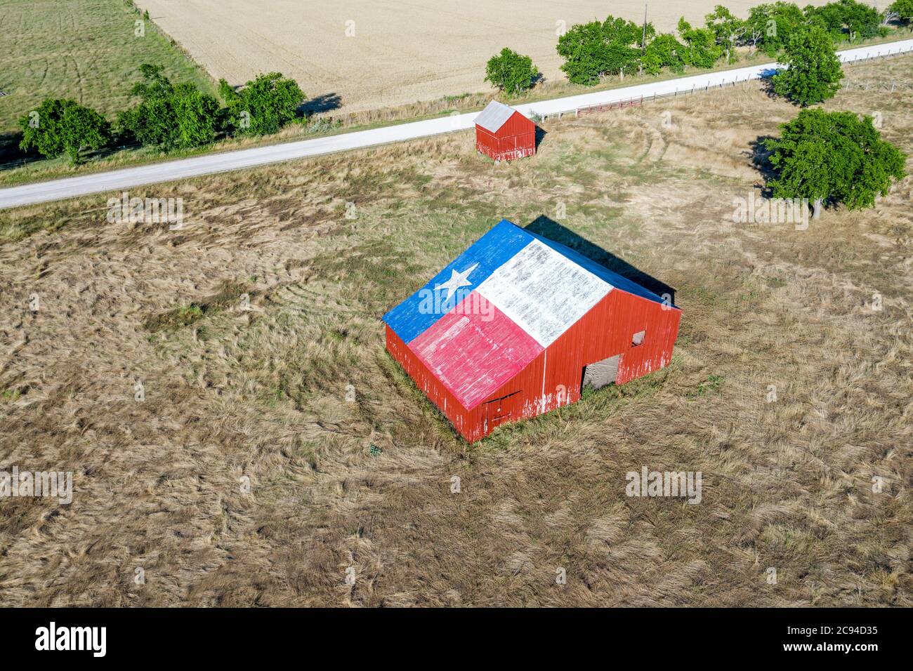 Un vecchio fienile abbandonato con il simbolo del Texas dipinto sul tetto si trova in una zona rurale dello stato, incorniciato da terreni agricoli. Foto Stock