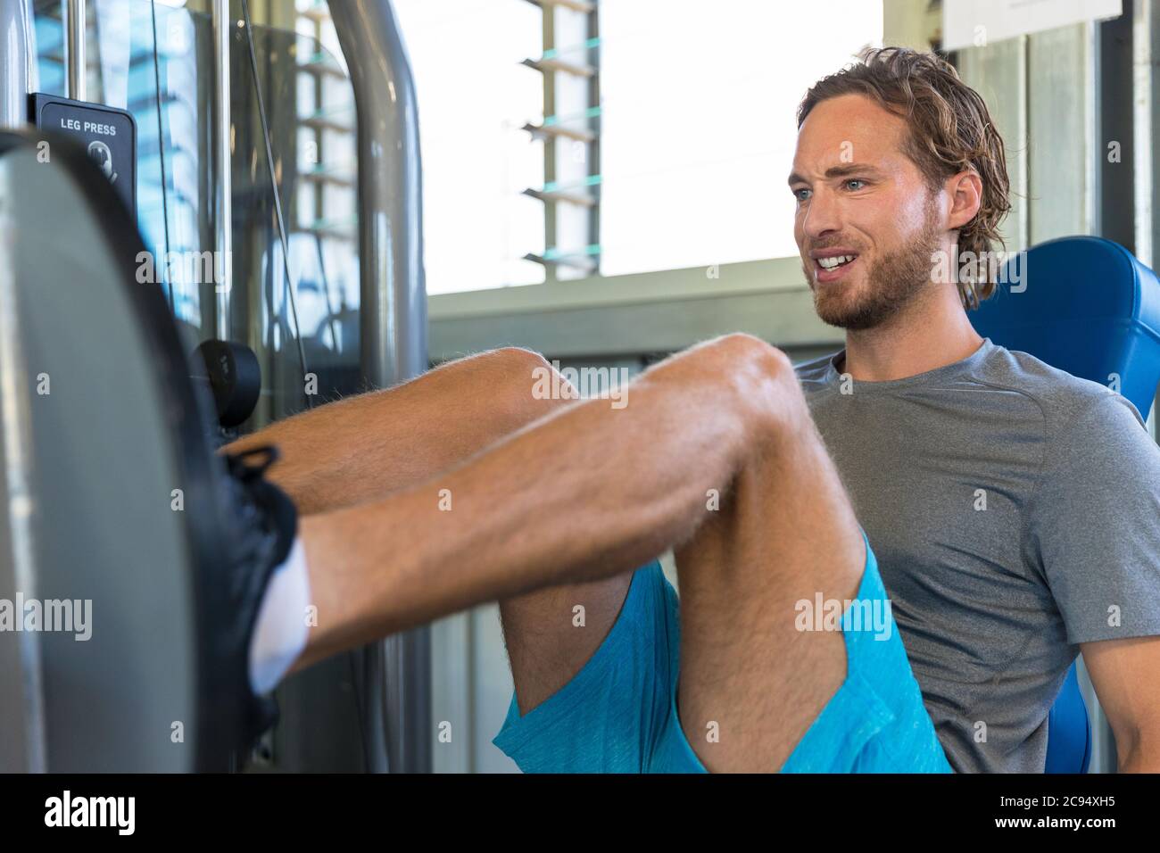 Palestra atleta che si allenano le gambe nel centro fitness. L'uomo che addestra i quads del corpo inferiore e i muscoli del hamstring usando la pressa della gamba Foto Stock