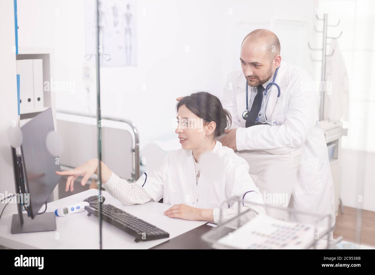 Team di giovani medici che lavorano insieme sul computer nella stanza dell'ospedale. Medici che indossano cappotti e stetoscopio. Foto Stock