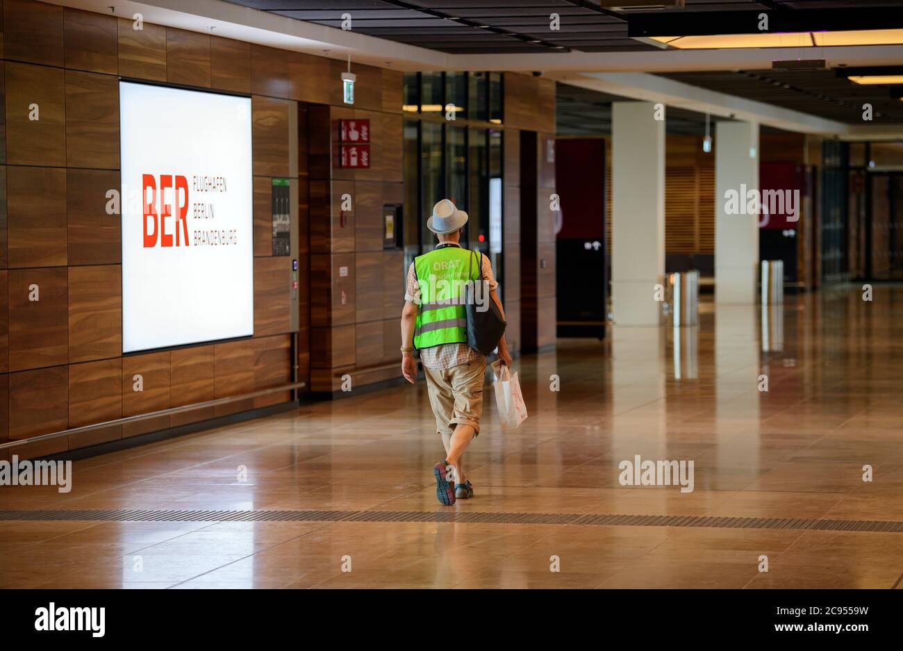 28 luglio 2020, Brandeburgo, Schönefeld: Un extra in un giubbotto verde ad alta visibilità passa attraverso il terminal dopo il controllo di sicurezza presso l'aeroporto di Berlino-Brandeburgo (BER). Nella seconda fase del trasferimento operazionale (ORAT), circa 500 - 600 dipendenti e 400 volontari hanno provato i processi standard dei passeggeri, dal check-in al controllo di sicurezza, imbarco e imbarco (arrivo). Foto: Soeren Stache/dpa-Zentralbild/dpa Foto Stock