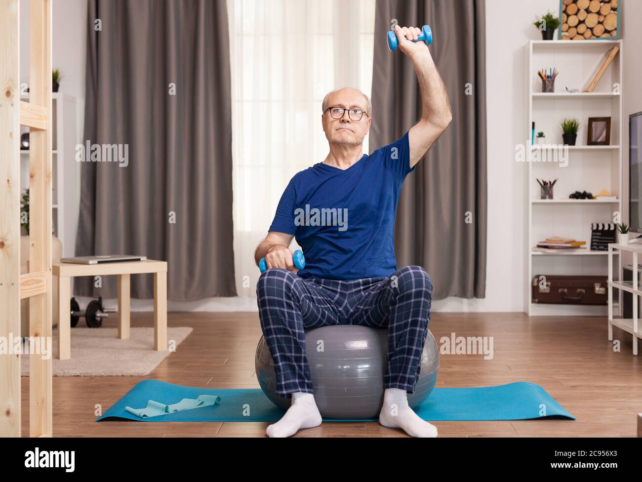 Nonno che usa i dumbbells essendo attento con la sua salute. Anziano pensionato online internet esercizio di formazione a casa attività sportiva con manubri, banda di resistenza, palla svizzera all'età di anziano pensionamento. Foto Stock