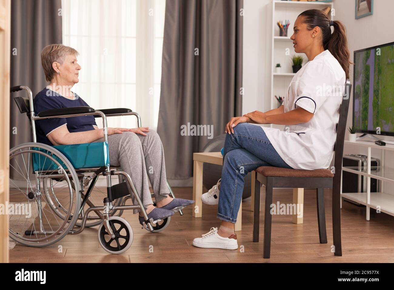Operatore sanitario che parla con una donna disabile seduta in sedia a rotelle. Disabile anziano ricoverato infermiera di aiuto professionale, cura di casa di riposo e riabilitazione Foto Stock