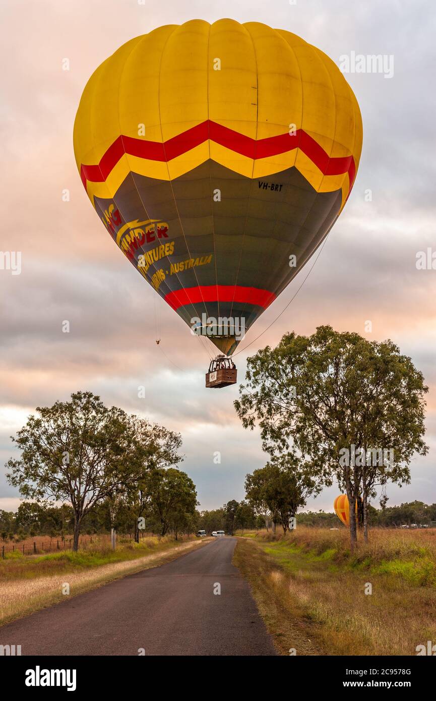 Un mongolfiera colorato con turisti, inizia la sua avventura all'alba che si innalza lentamente sopra gli alberi e una strada di campagna a Mareba, Queensland, Australia. Foto Stock