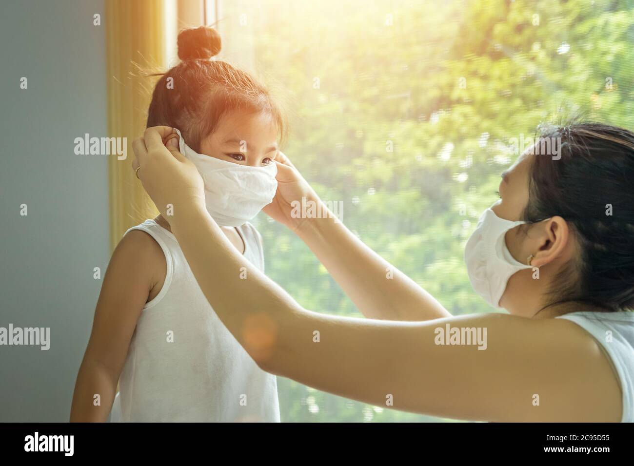 Famiglia asiatica con bambini in maschera di faccia, madre si prepara a mettere la maschera di faccia sul suo bambino prima di lasciare casa per andare a scuola per prevenire i germi Foto Stock