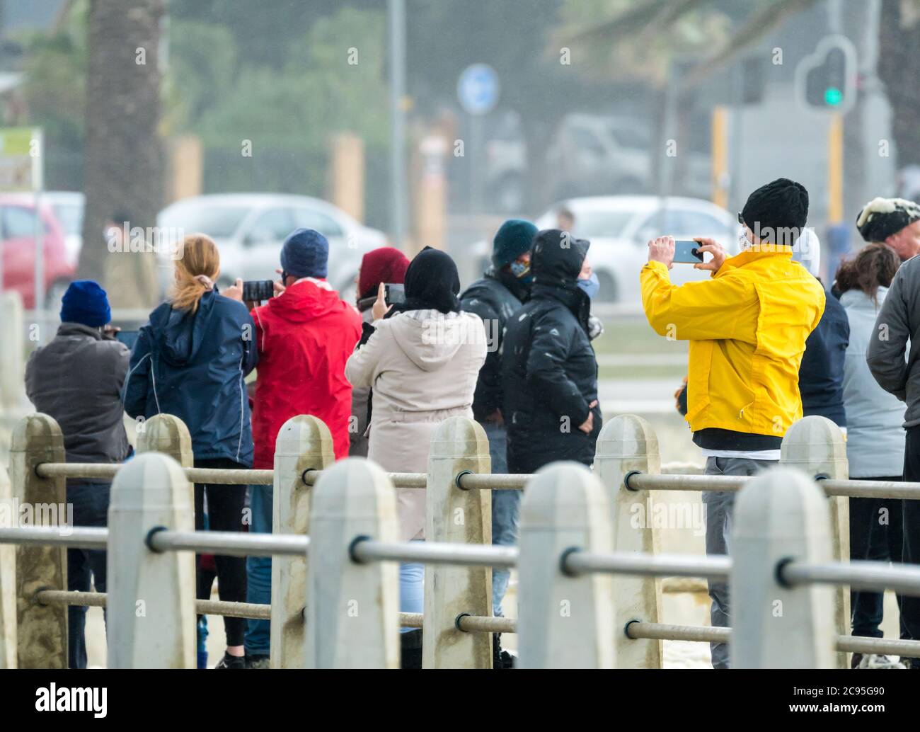Folla o gruppo di persone vestite di abbigliamento invernale che scatta foto di un fenomeno meteorologico durante una tempesta a Città del Capo, Sud Africa. Concetto di clima Foto Stock