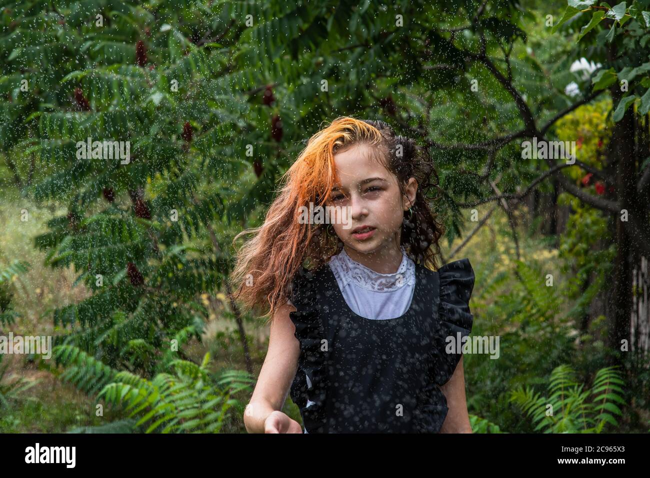 Ragazzina umida in piedi sotto la pioggia. Adolescente in uniforme scolastica in primavera o autunno caldo. Ragazza di 5° grado. Colorazione dei capelli. Foto Stock