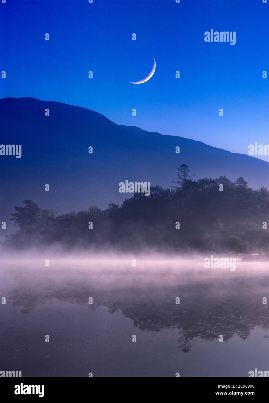 Nebbia di mattina presto sul lago con grande luna crescente Foto Stock
