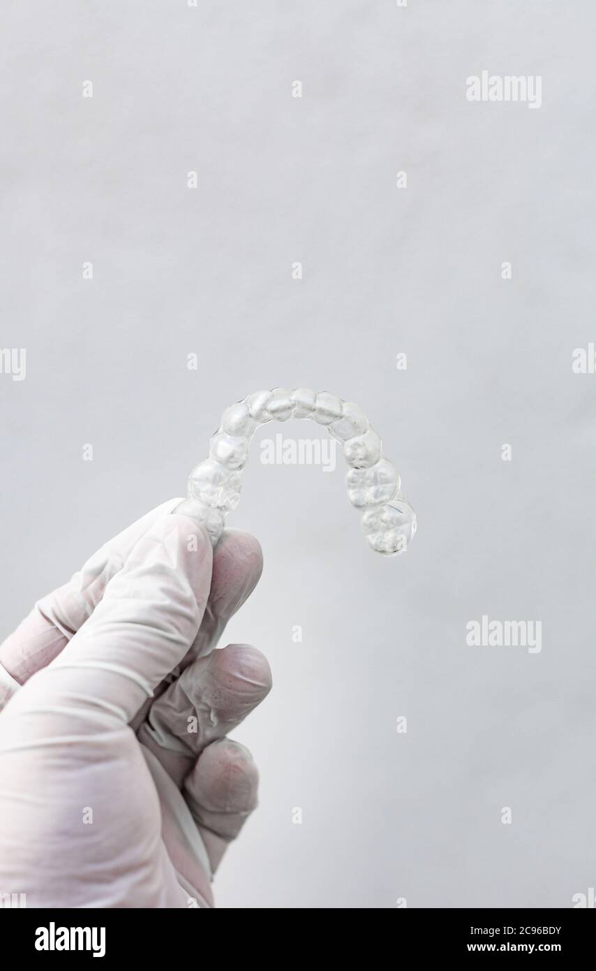 Bretelle dentali invisibili su sfondo bianco tenute da una mano con guanto igienico Foto Stock