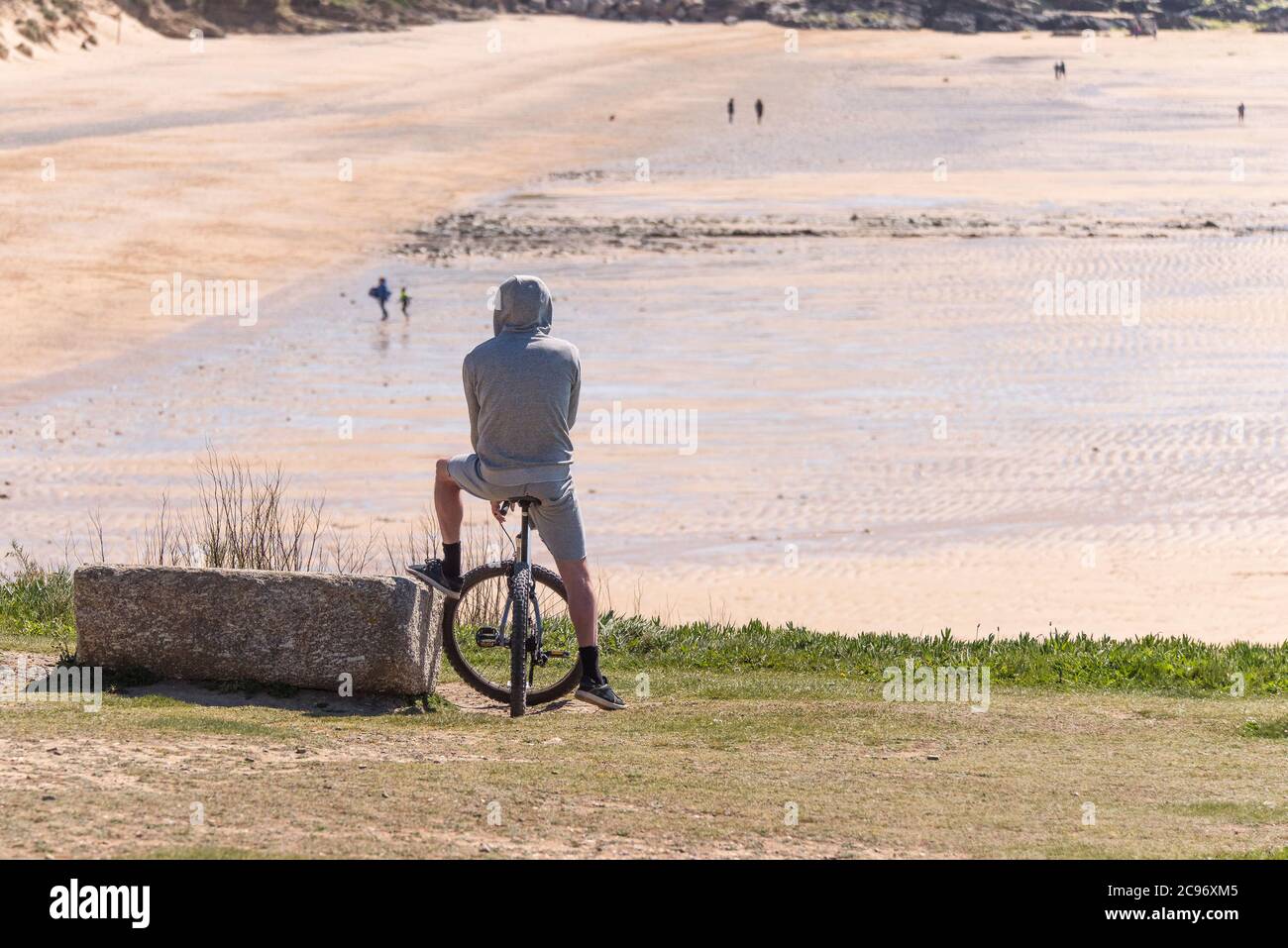 Un uomo che indossa una felpa con cappuccio seduto sulla sua mountain bike  con vista sulla spiaggia di Fistral a Newquay in Cornovaglia Foto stock -  Alamy