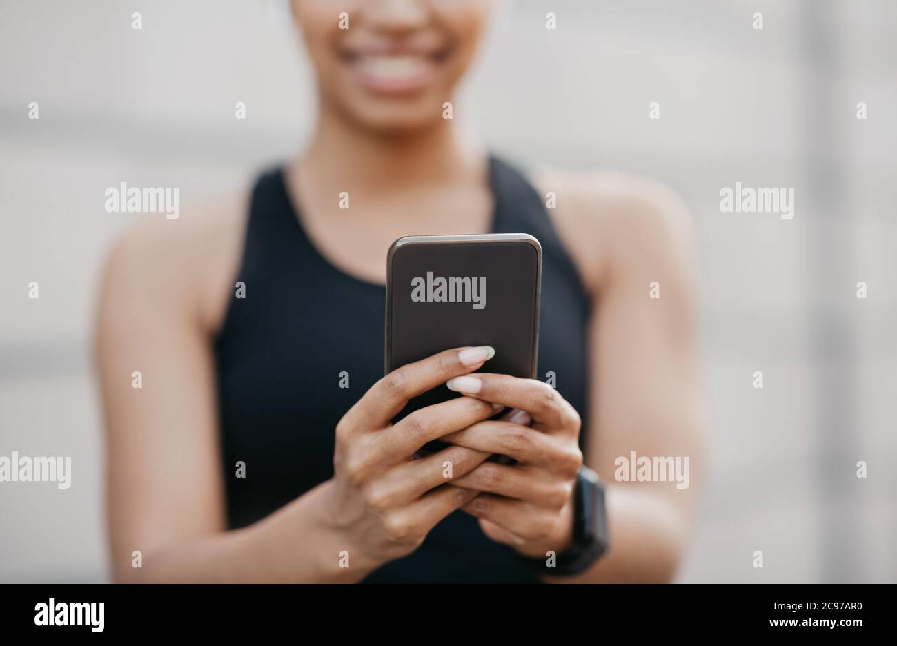 Sport e reti sociali. Donna sorridente in abbigliamento sportivo con fitness tracker digitando su smartphone Foto Stock
