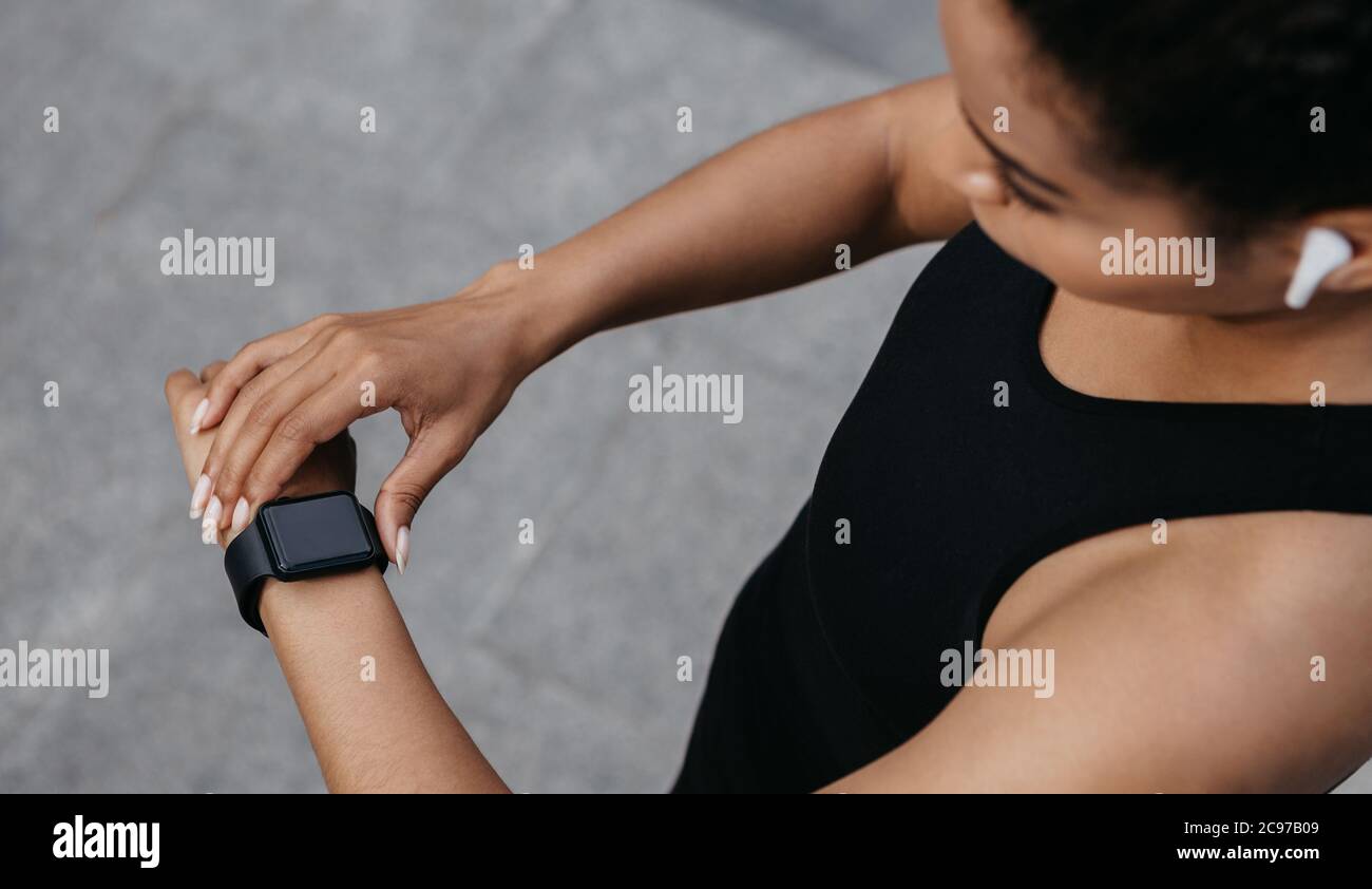 Corsa e frequenza cardiaca. Donna controlla fitness tracker sul braccio, jogging con cuffie wireless Foto Stock