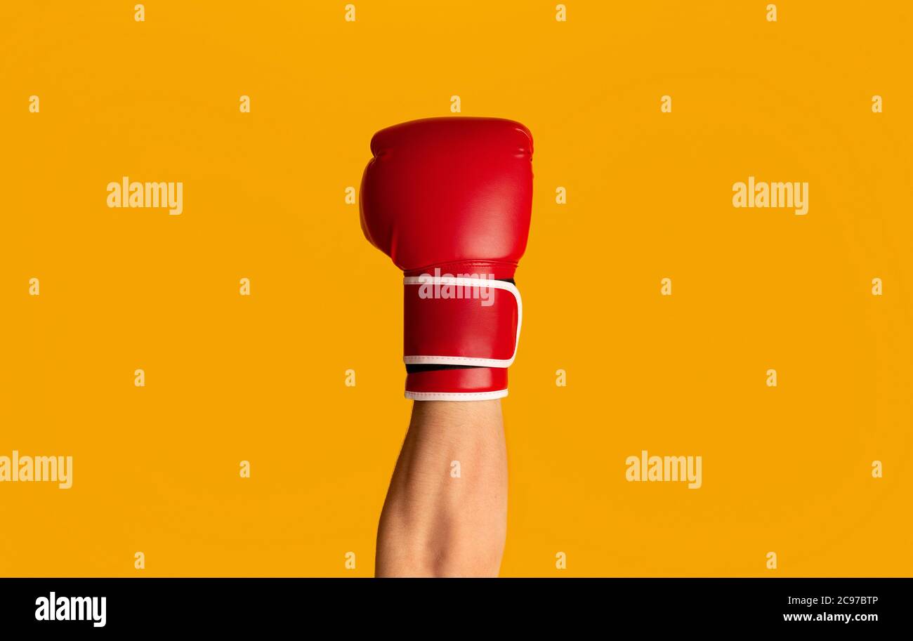 Sportivo che indossa guanto da boxe su sfondo arancione, primo piano di mano Foto Stock