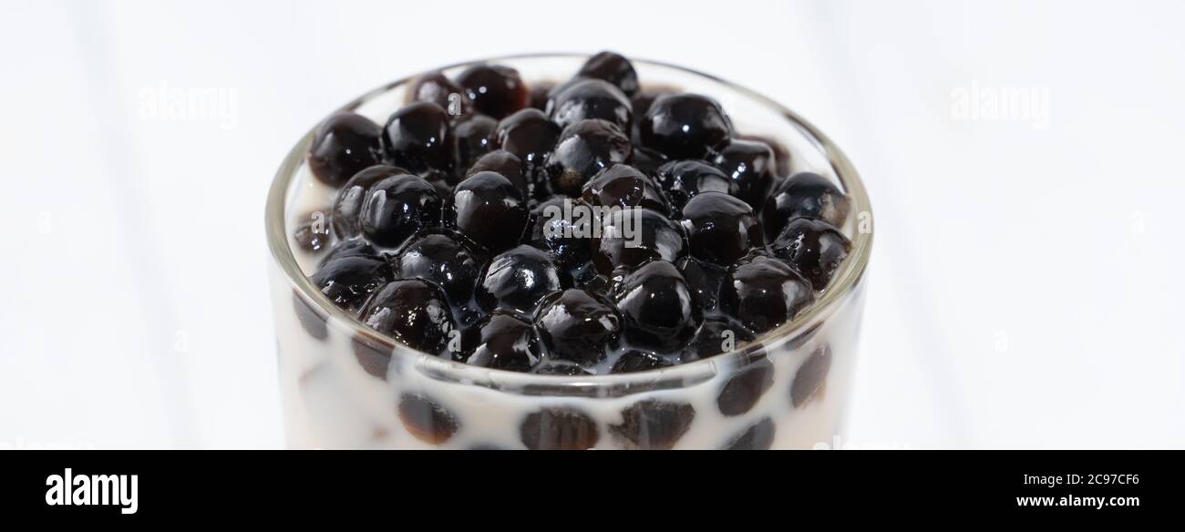Tè al latte con tatuetta di tapioca, famosa bevanda taiwanese su sfondo bianco di legno in vetro da bere, primo piano, spazio per le copie Foto Stock