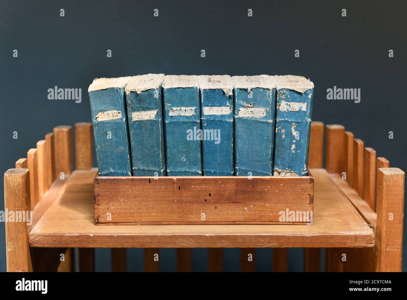 Set di vecchi libri d'epoca usurati e distrutti con spine blu ed etichette su una mensola di legno contro una parete grigia Foto Stock