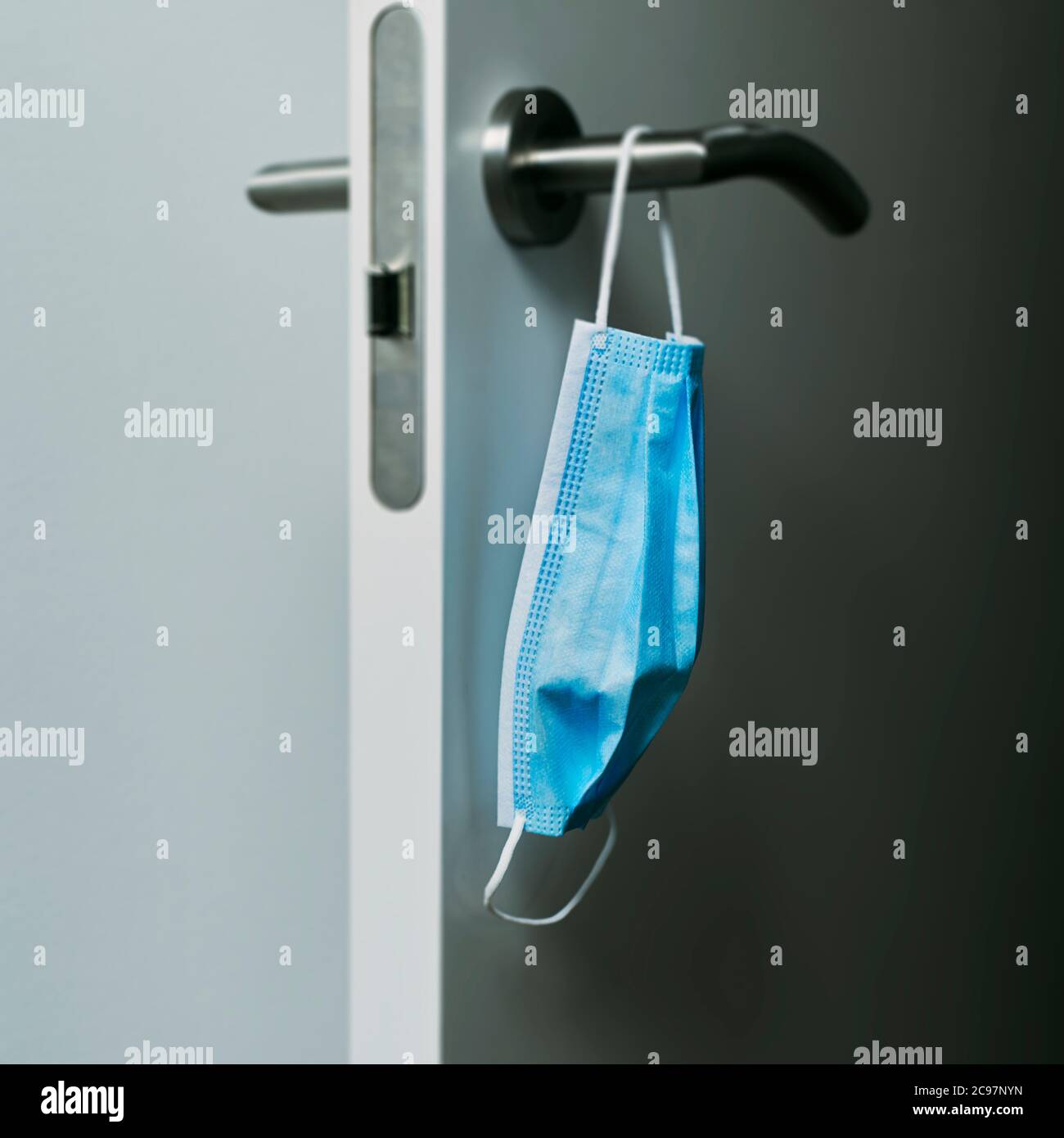 chiusura di una maschera chirurgica blu appesa al moderno pomello di una porta aperta Foto Stock