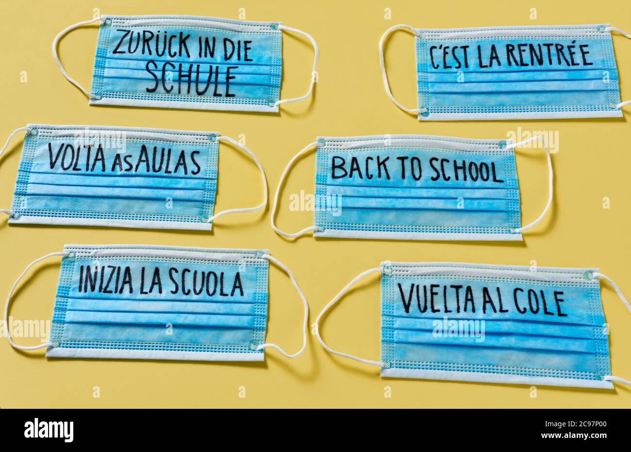 maschera chirurgica con il testo di ritorno a scuola scritto in tedesco, inglese, portoghese, francese, italiano e spagnolo, raffigurante la necessità di prevenire l'infe Foto Stock