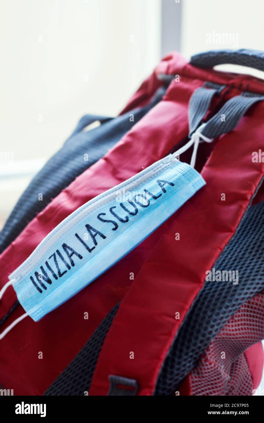 chiusura di una libreria rossa e grigia e di una maschera chirurgica blu con il testo di ritorno a scuola scritto in italiano, che raffigura la necessità di prevenire l'infettio Foto Stock