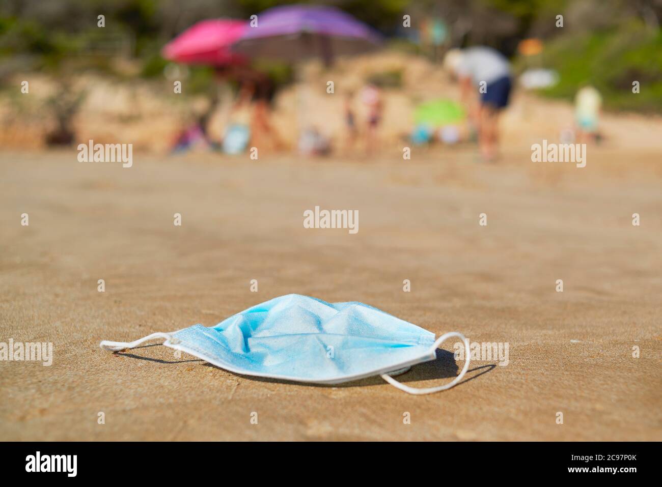 primo piano di una maschera chirurgica blu usata gettata sulla sabbia bagnata della riva di una spiaggia Foto Stock
