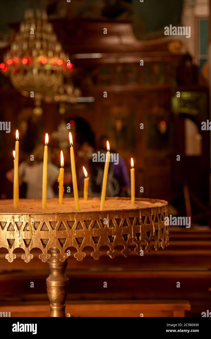 Primo piano immagine di candele poste su una prova di metallo e accese durante un'osservanza religiosa. E' un'immagine interna a bassa luce che caratterizza le persone che pregano e un Foto Stock