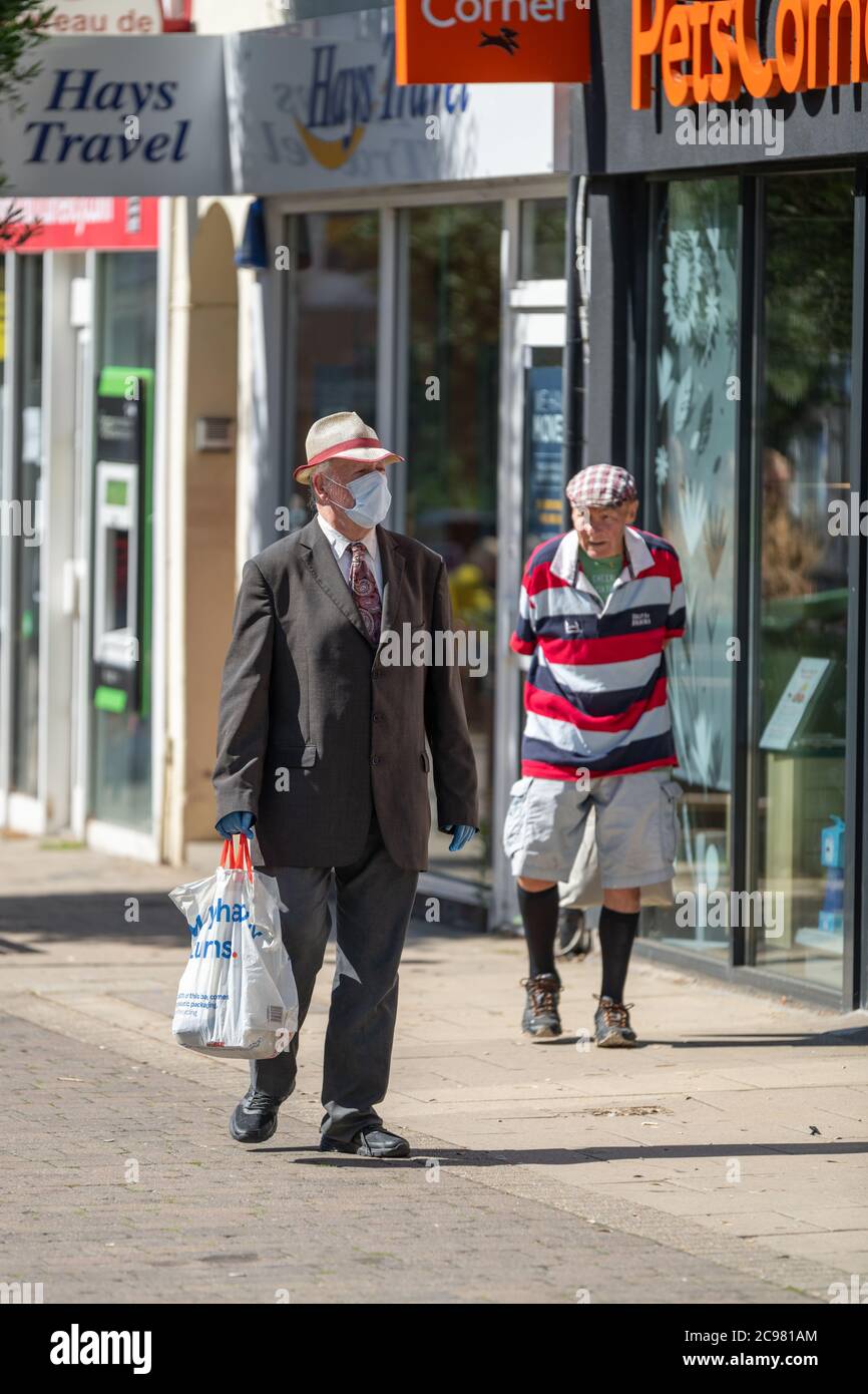 Un pensionato che indossa una maschera facciale e guanti in lattice cammina lungo una strada pedonale. George Street, Hove, East Sussex, Regno Unito. Foto Stock