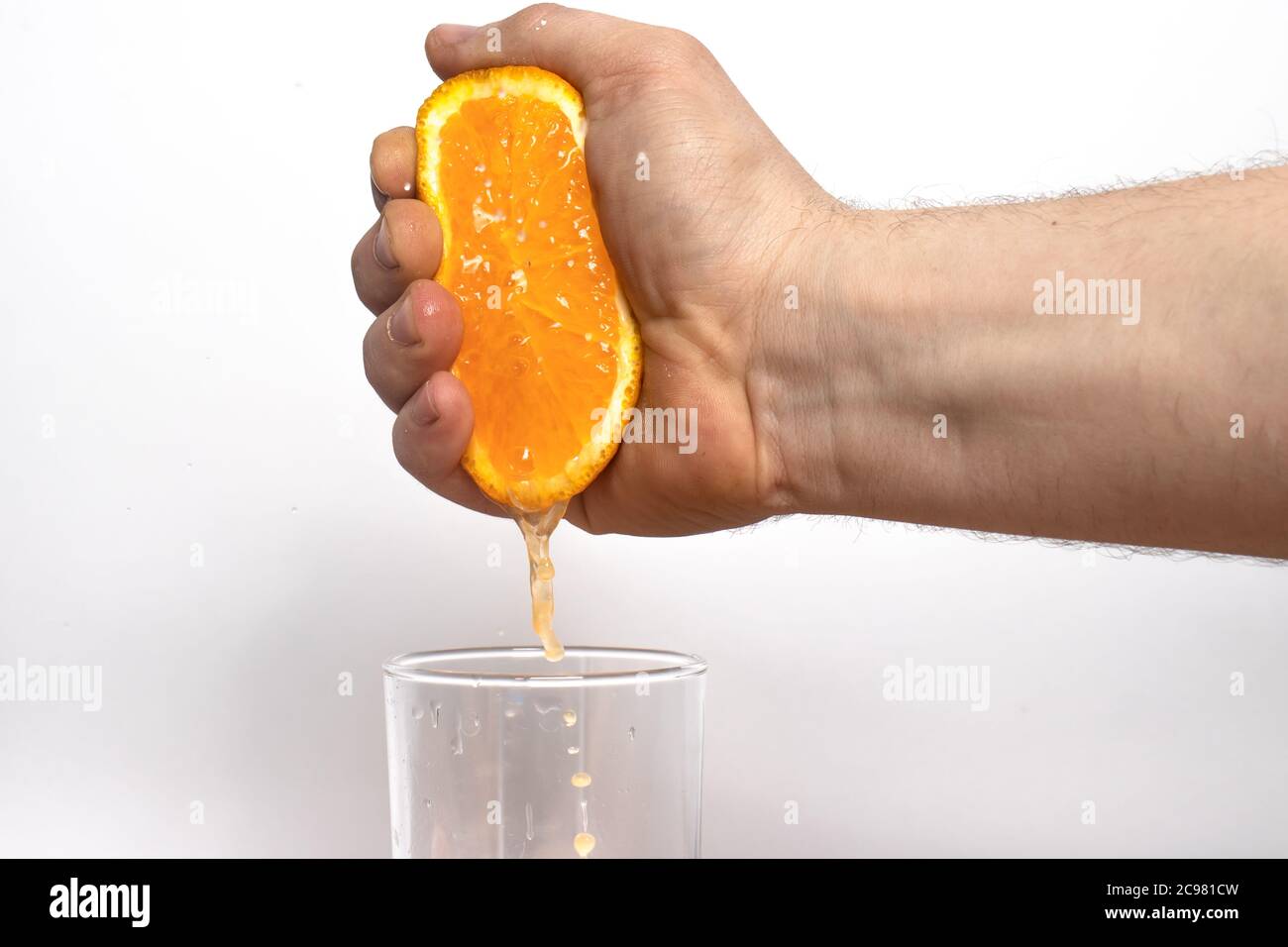 Un uomo spreme il succo di un'arancia matura succosa. La mano maschile preme il succo d'arancia in un bicchiere su sfondo bianco. Foto Stock