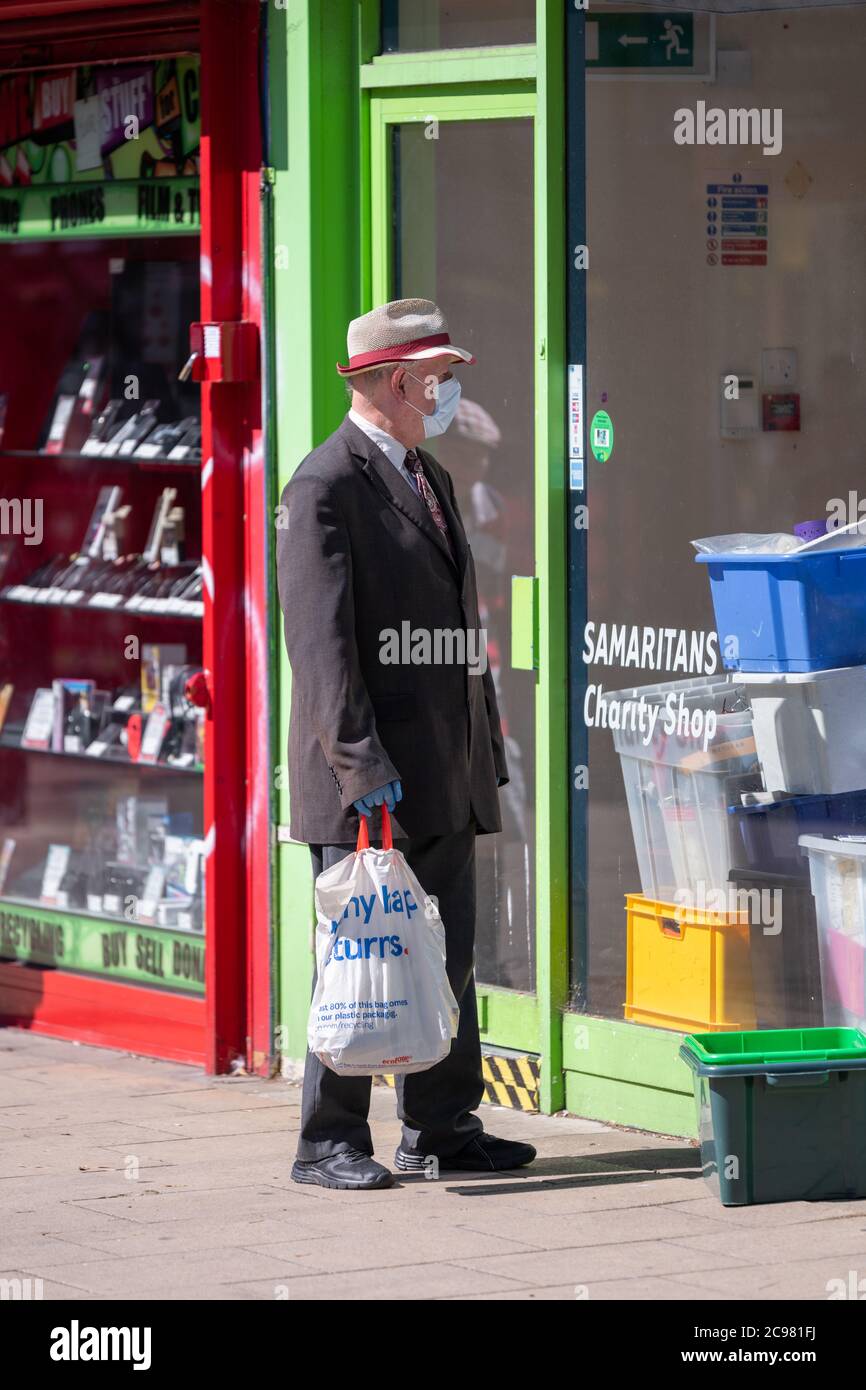 Un pensionato che indossa una maschera facciale e guanti in lattice guarda alla finestra di un negozio di beneficenza. George Street, Hove, East Sussex, Regno Unito. Foto Stock